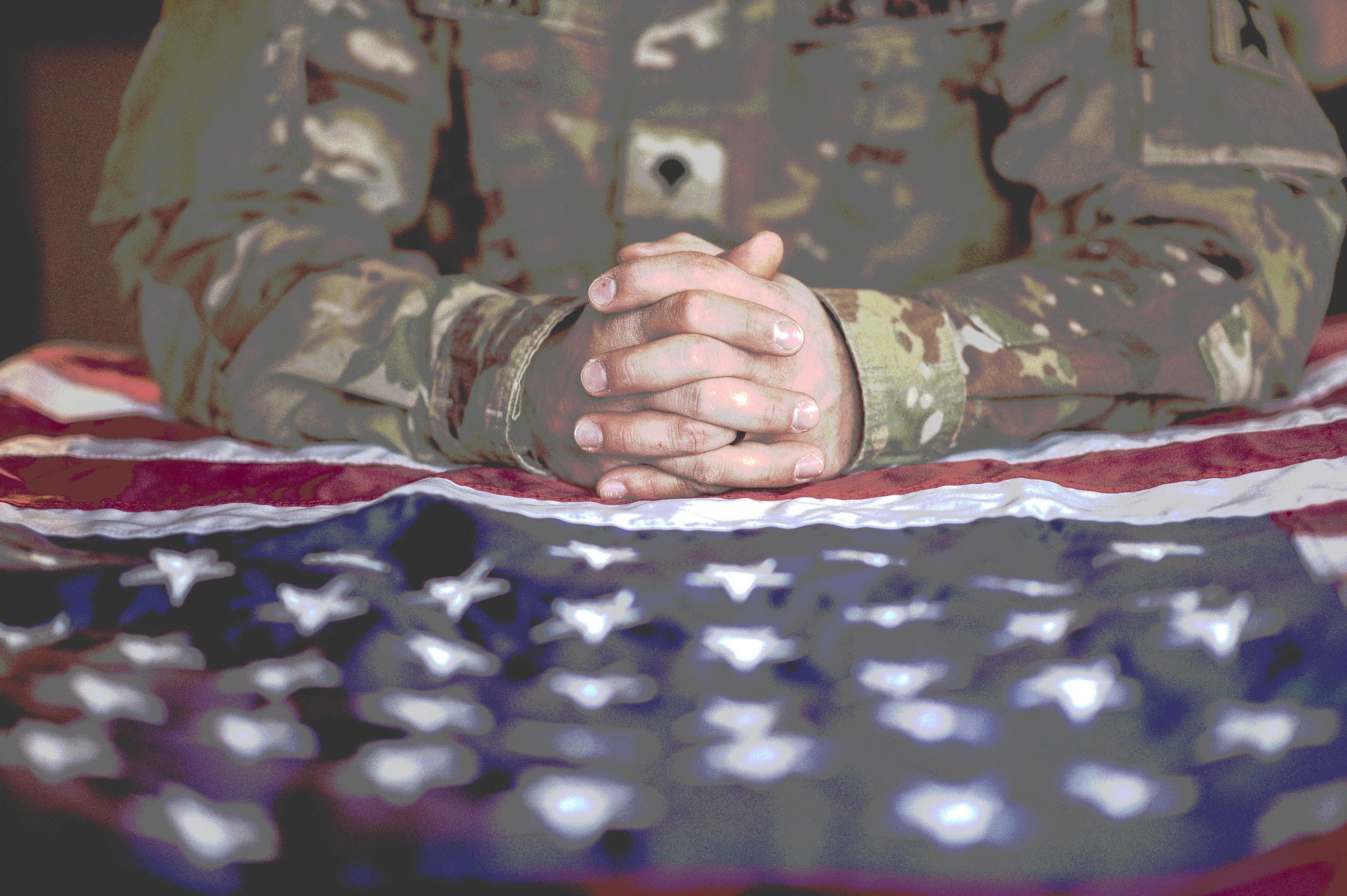American soldier mourning and praying with the American flag in front of him